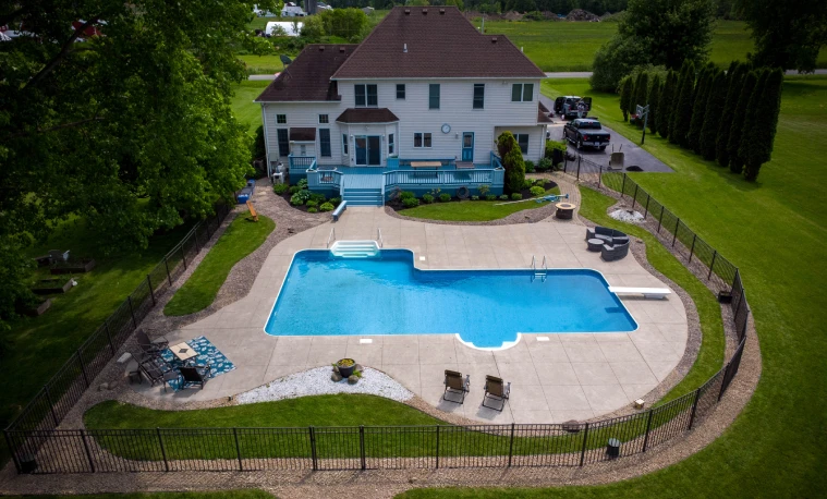 Aerial view of a backyard with an in-ground pool, patio, and landscaped beds